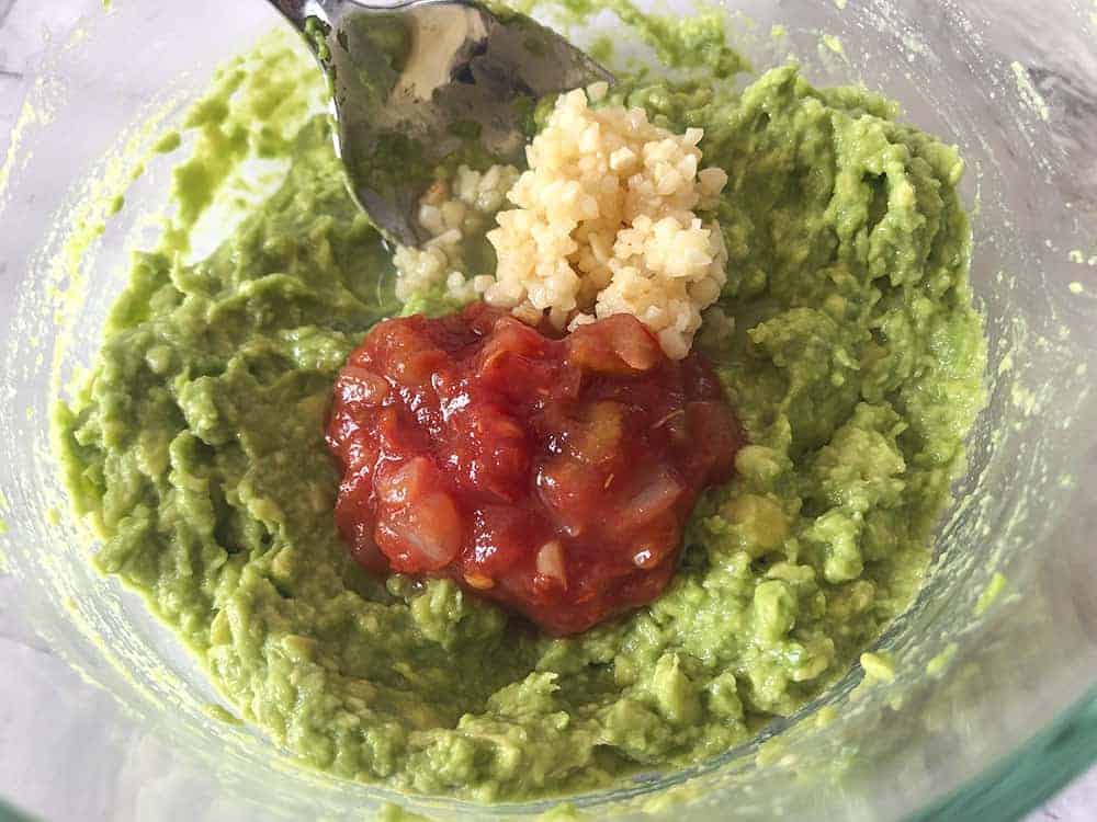 Mashed avocadoes with the salsa and the garlic sitting on top, ready to mix in. 
