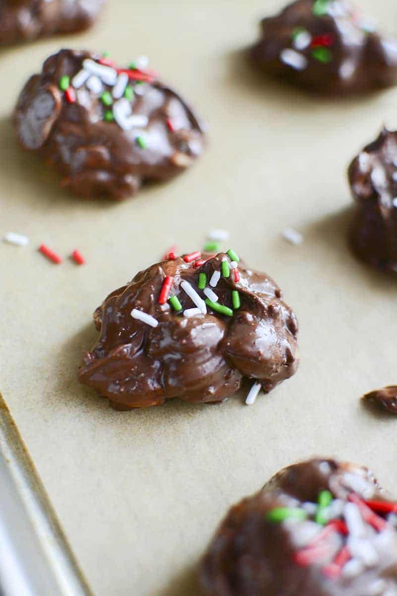 The chocolate covered nuts drying on parchment paper with red, white and green sprinkles on top.