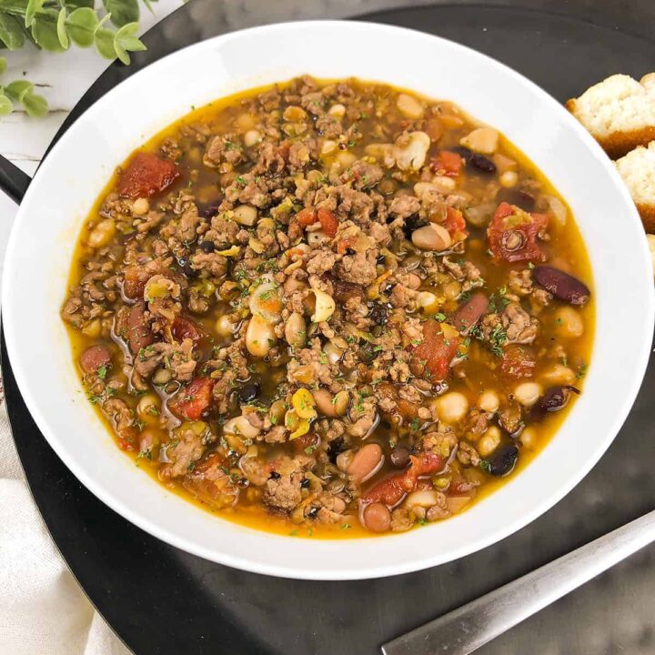 Slow cooker bean soup in a white bowl that's sitting on a black tray.