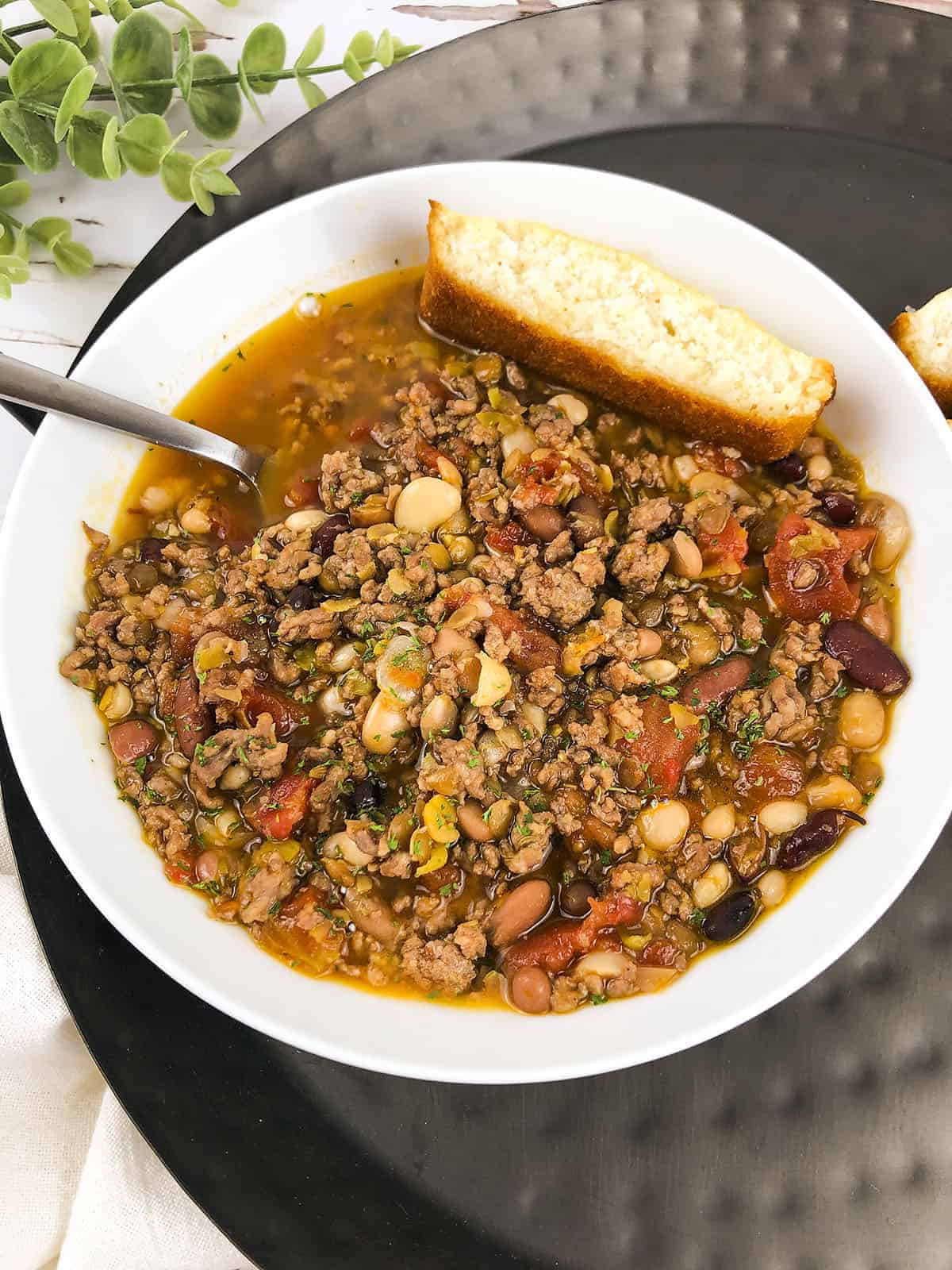 The 15 bean soup with a piece of cornbread at the top. A spoon is sticking out on the left side.