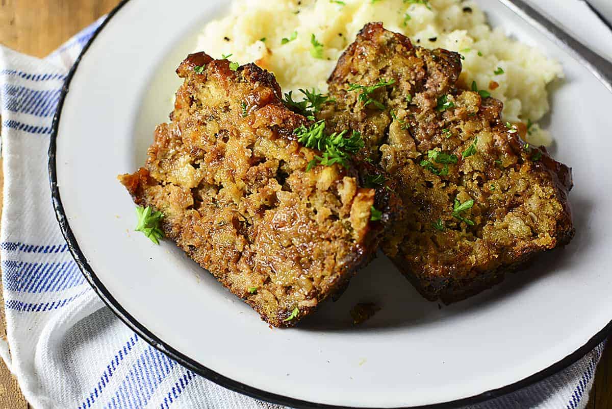 Two pieces of meatloaf sitting on a plate with mashed potatoes.