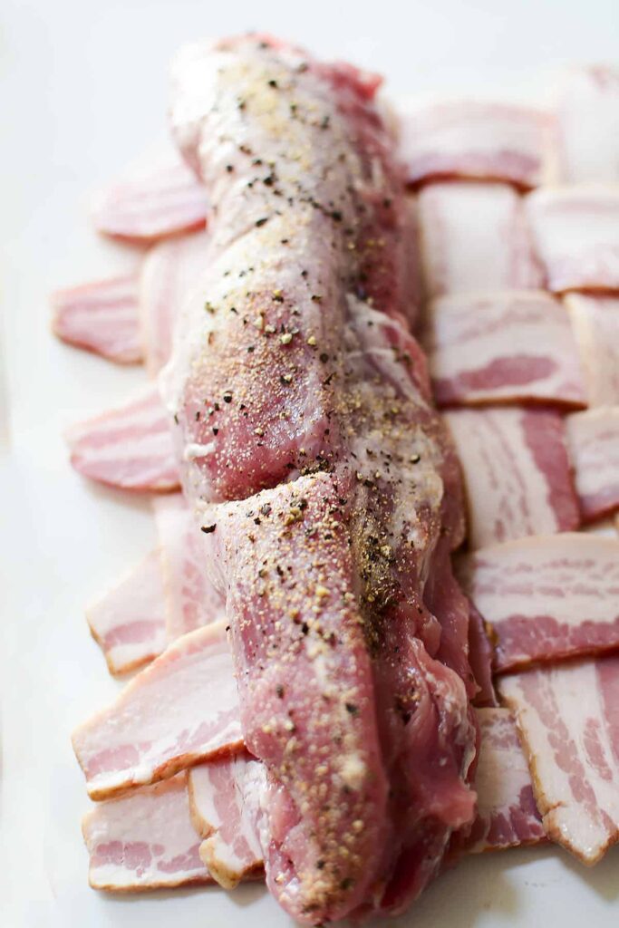Seasoned pork tenderoin about to wrapped in a bacon weave.