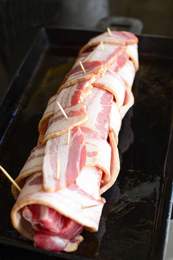 Pork tenderloin wrapped in bacon in a cast iron pan.