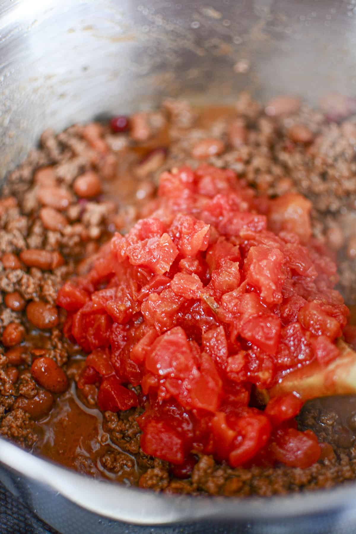 Rotel is added to the ground beef in the pot.