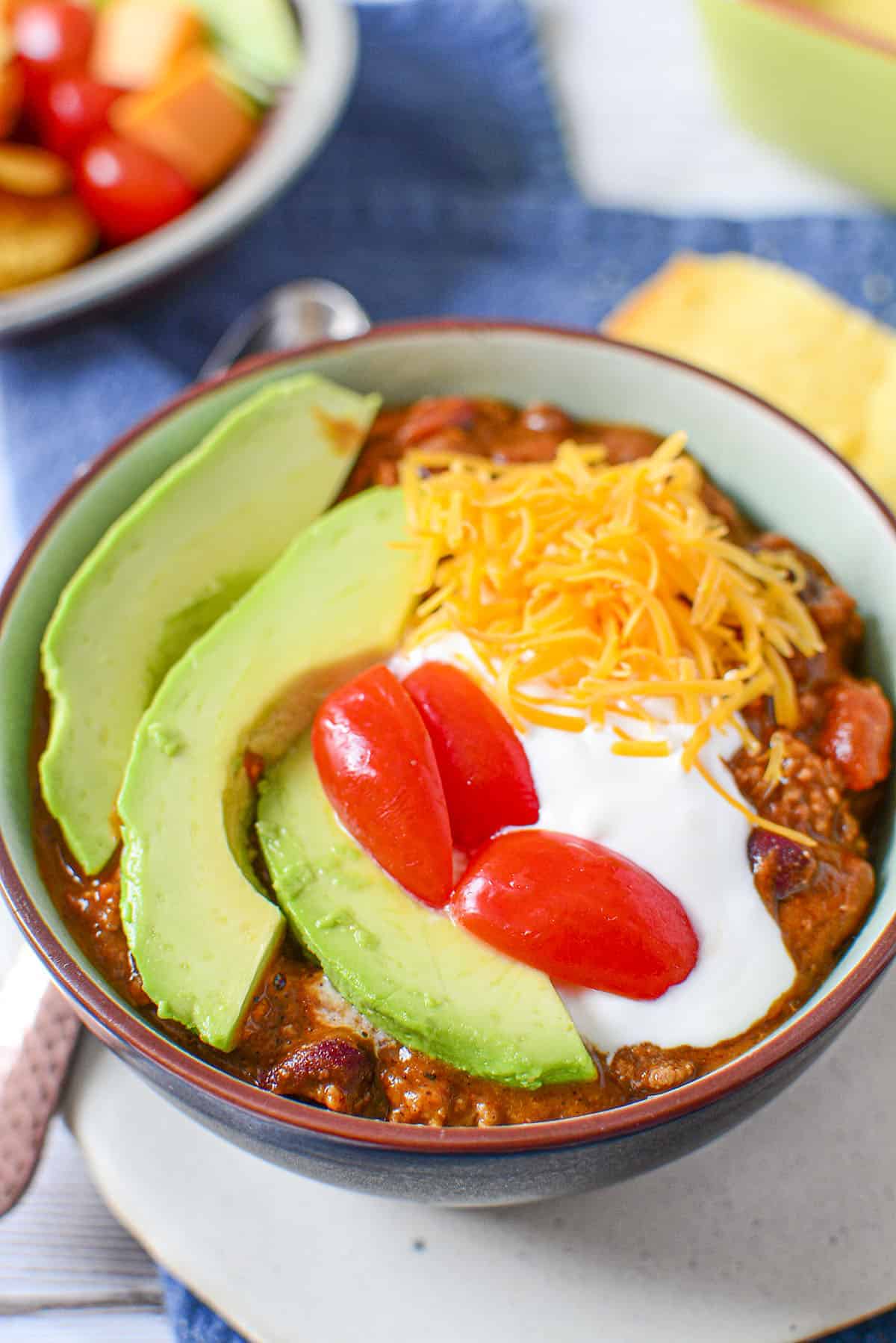 A bowl of chili with avocado, tomatoes, sour cream and cheese.