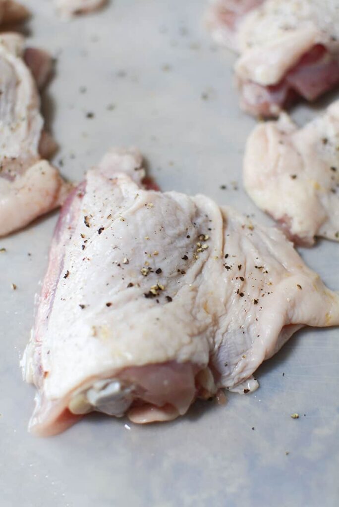 Raw chicken thigh with salt, pepper and garlic powder sprinkled over it.