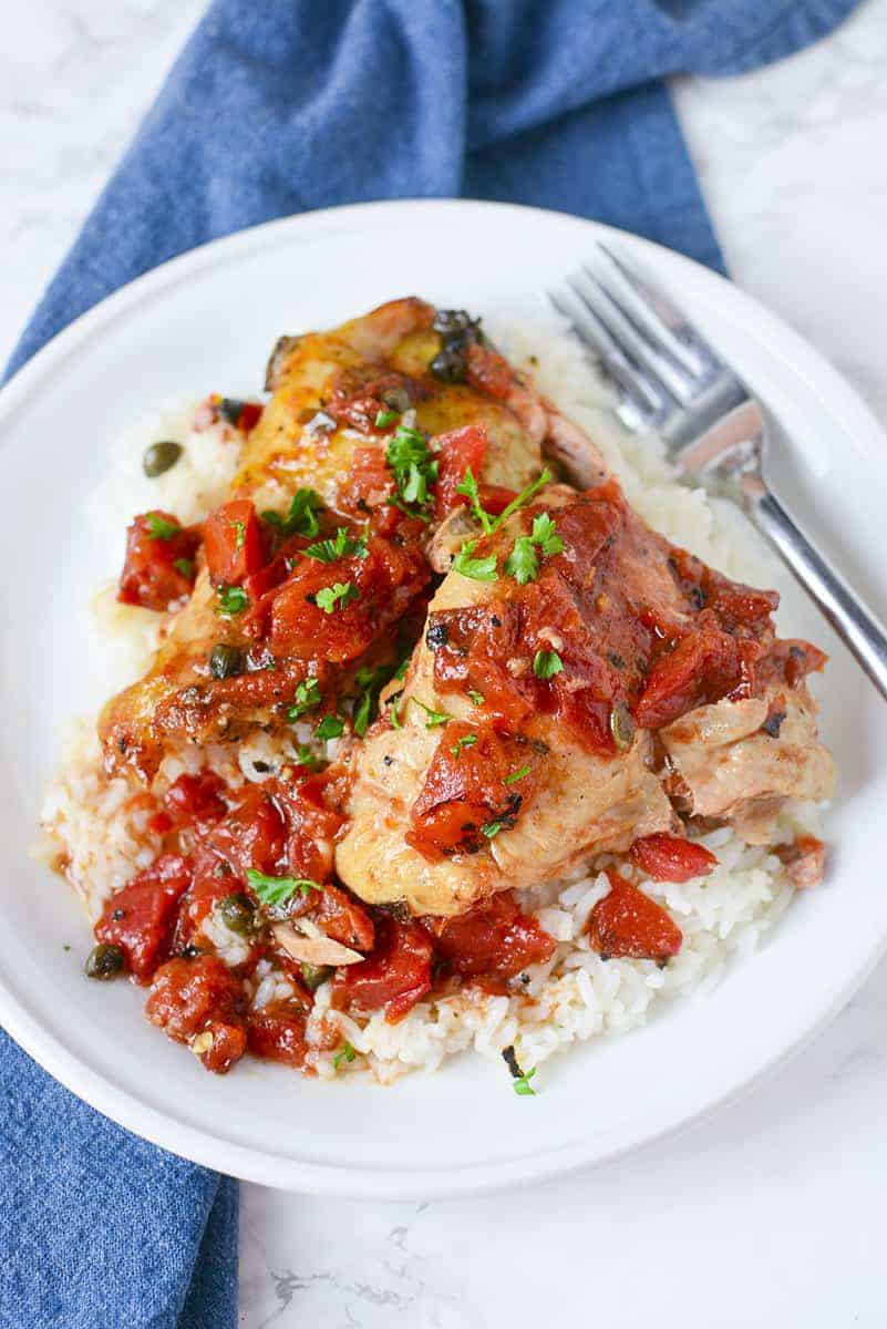 Crockpot tuscan chicken on a white plate with a fork on the right side.