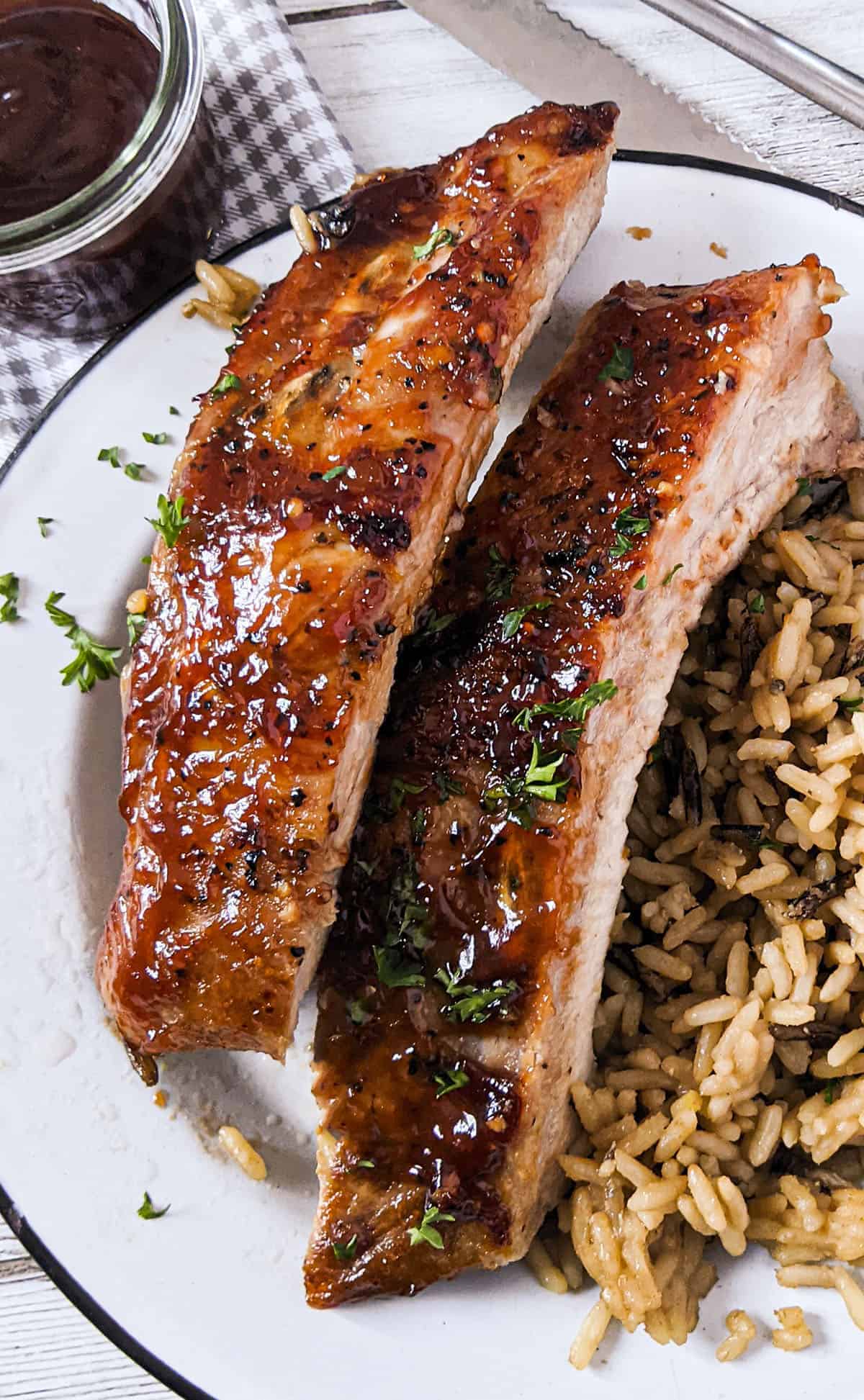 2 oven roasted ribs on a white plate with rice on the side.