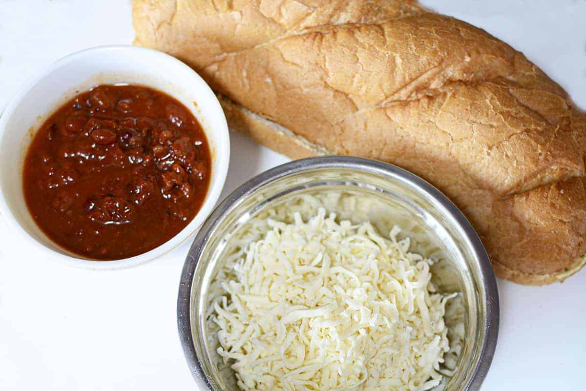 Chili, shredded mozza and a garlic bread loaf on a white background.