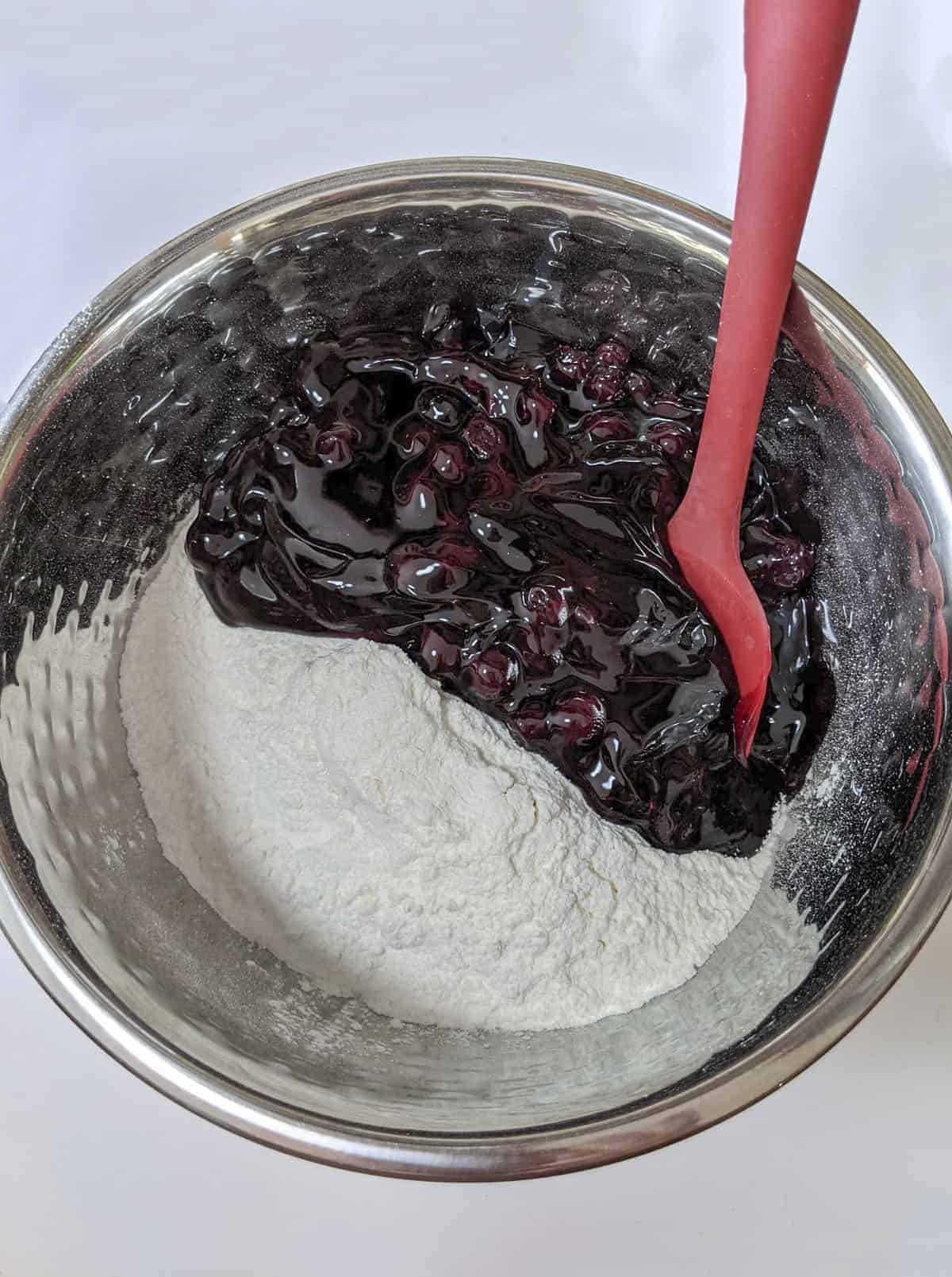 Blueberry pie filling and cake mix sitting in a bowl with a red spatula on the right.