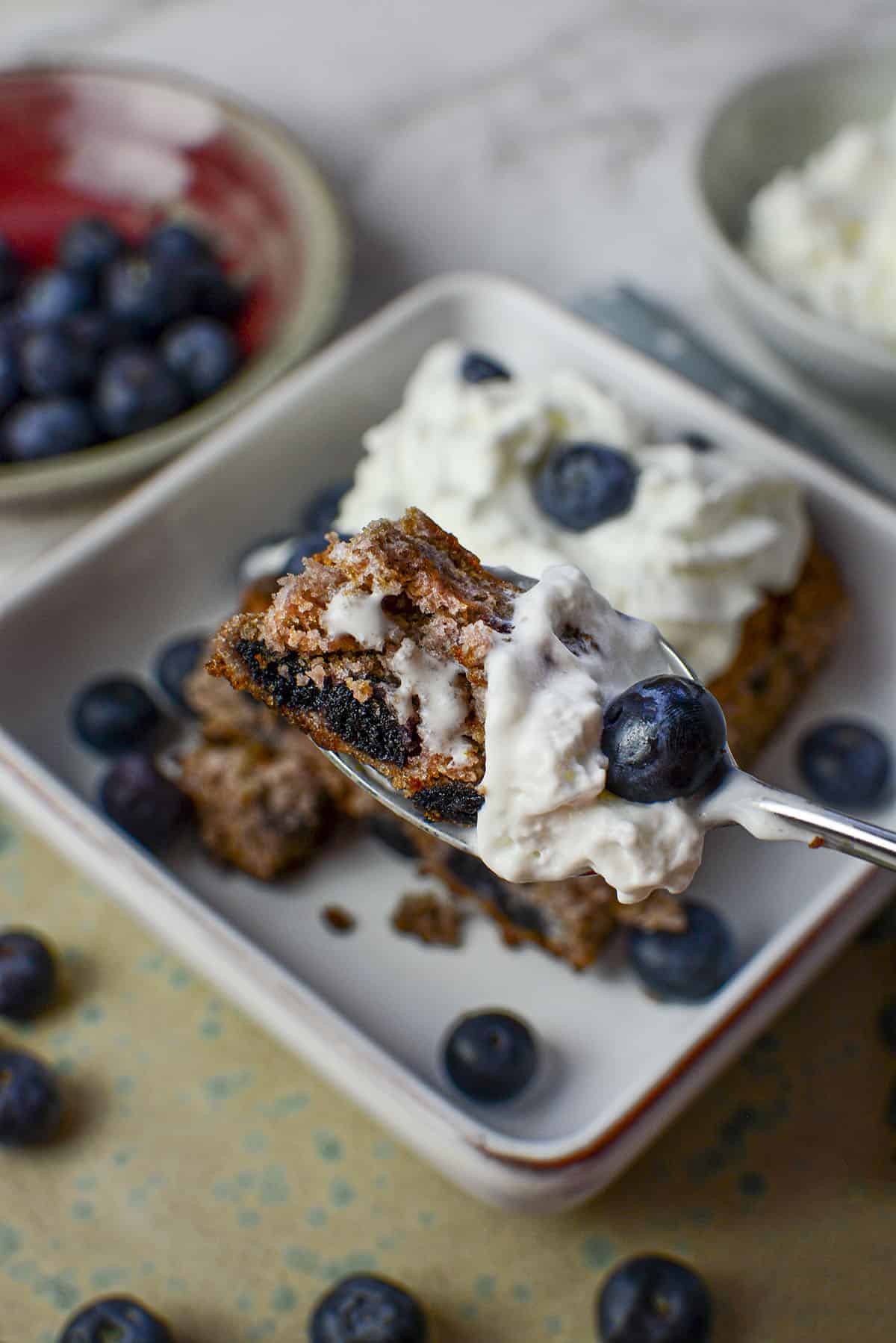 A spoonful bite of the blueberry cake with whipped cream and fresh blueberries.