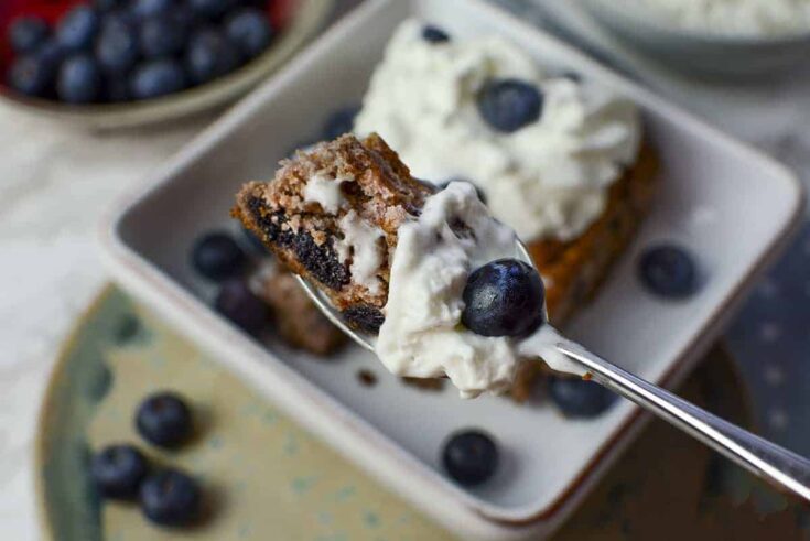 A spoonful of blueberry cake with whipped cream and fresh blueberries.