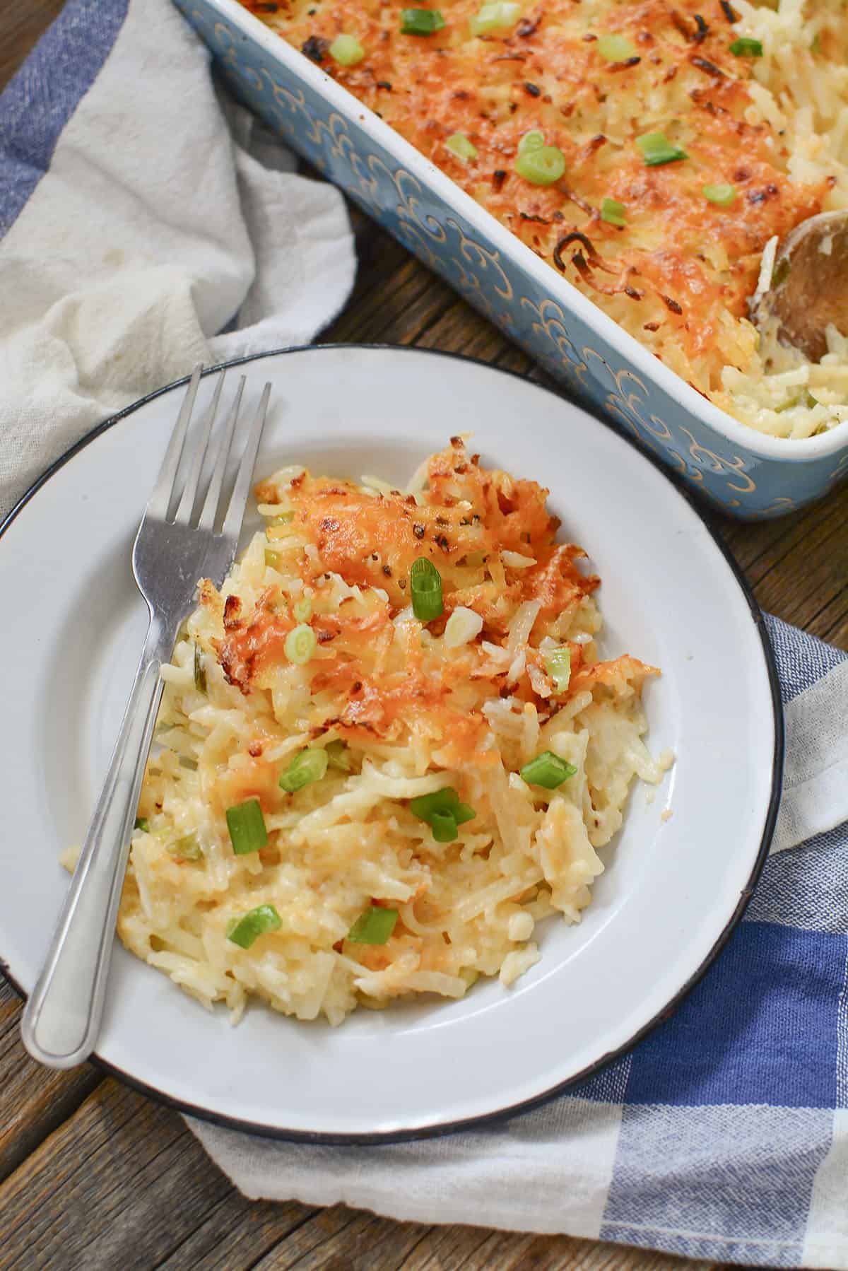 Creamy hash brown casserole on a white plate on a blue napkin.