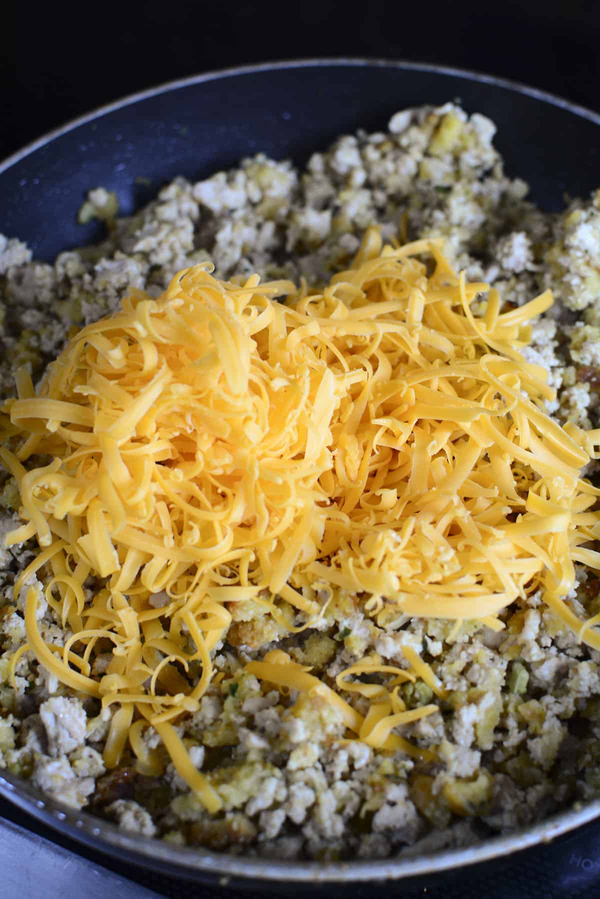 Adding the shredded cheese on top of the chicken mixture.