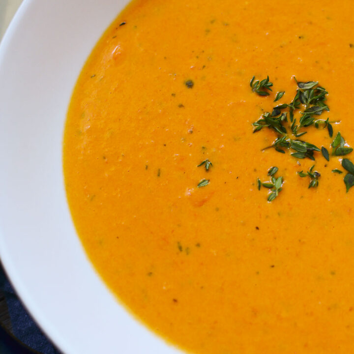 The left side of a bowl of Boursin Tomato soup in a bowl with Thyme sprinkled on top.