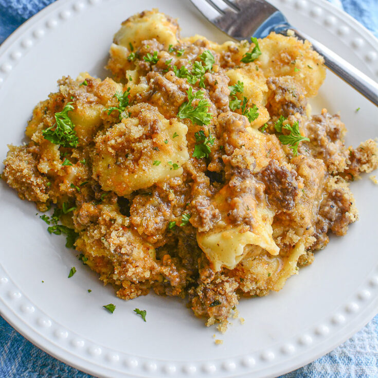 Delicious beefy tortellini mac and cheese ready to eat on a whilte plate with a fork.