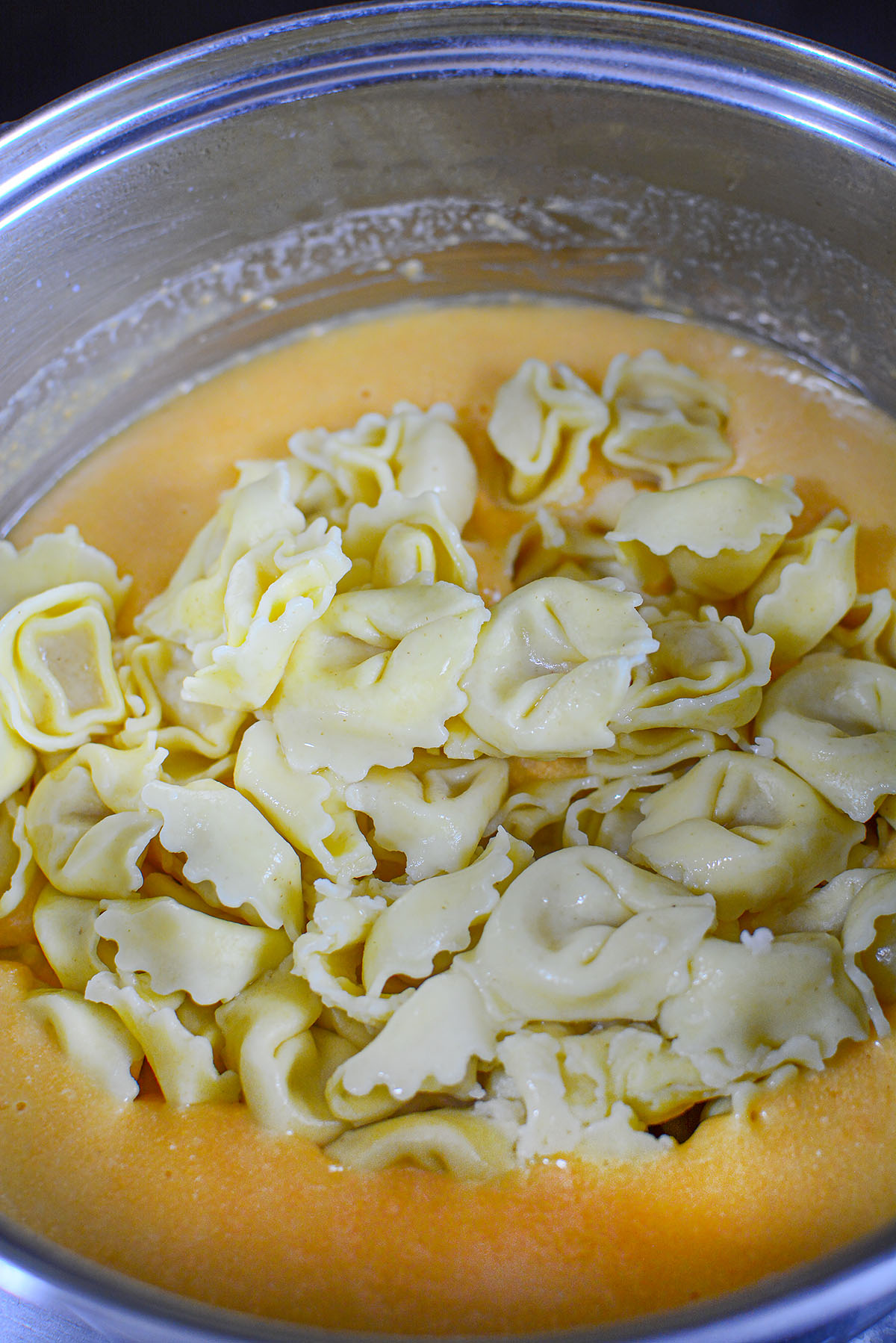 Adding cooked tortellini to the cheese sauce.