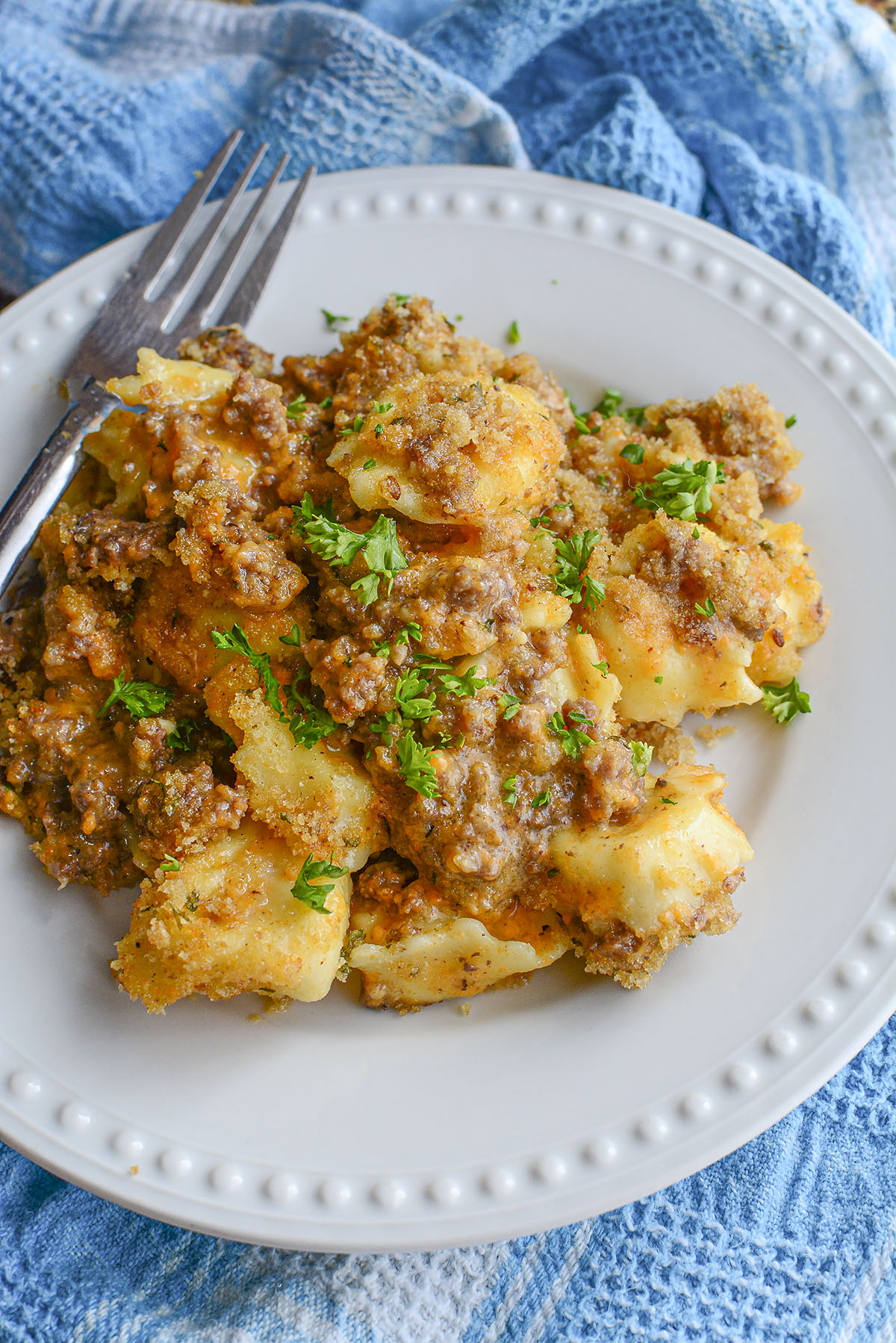 Beef and cheese tortellini mac and cheese sitting on a white plate with a fork to the left of the food.