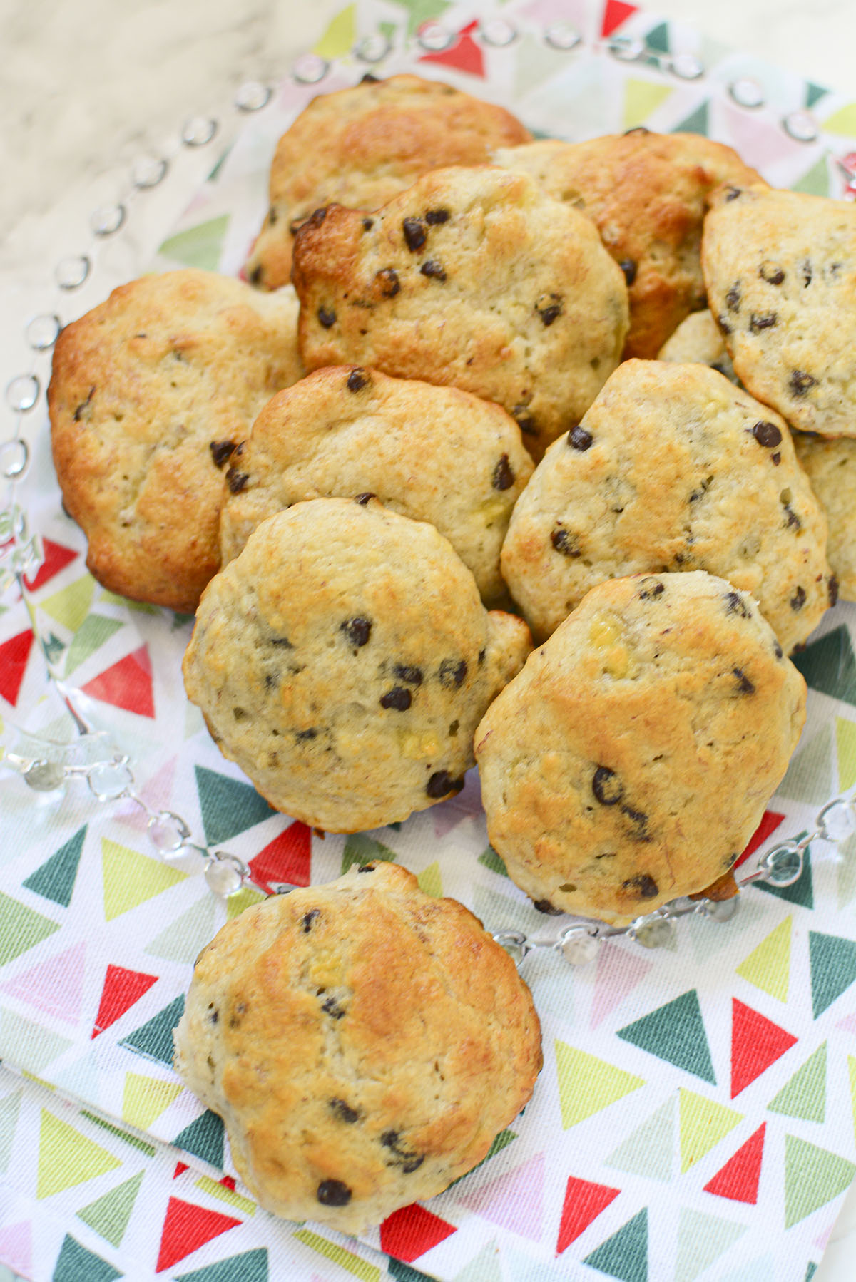 The banana chocolate chip cookies on a glass clear plate that's sitting on a colorful tea towel.