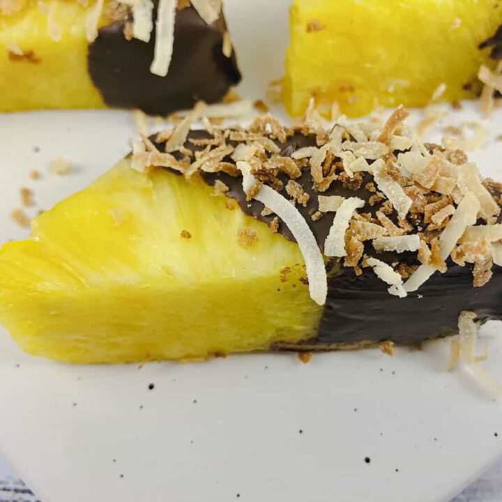 A pineapple spear covered in chocolate with toasted coconut over top.