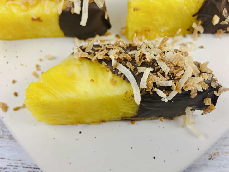 A pineapple spear covered in chocolate with toasted coconut over top.