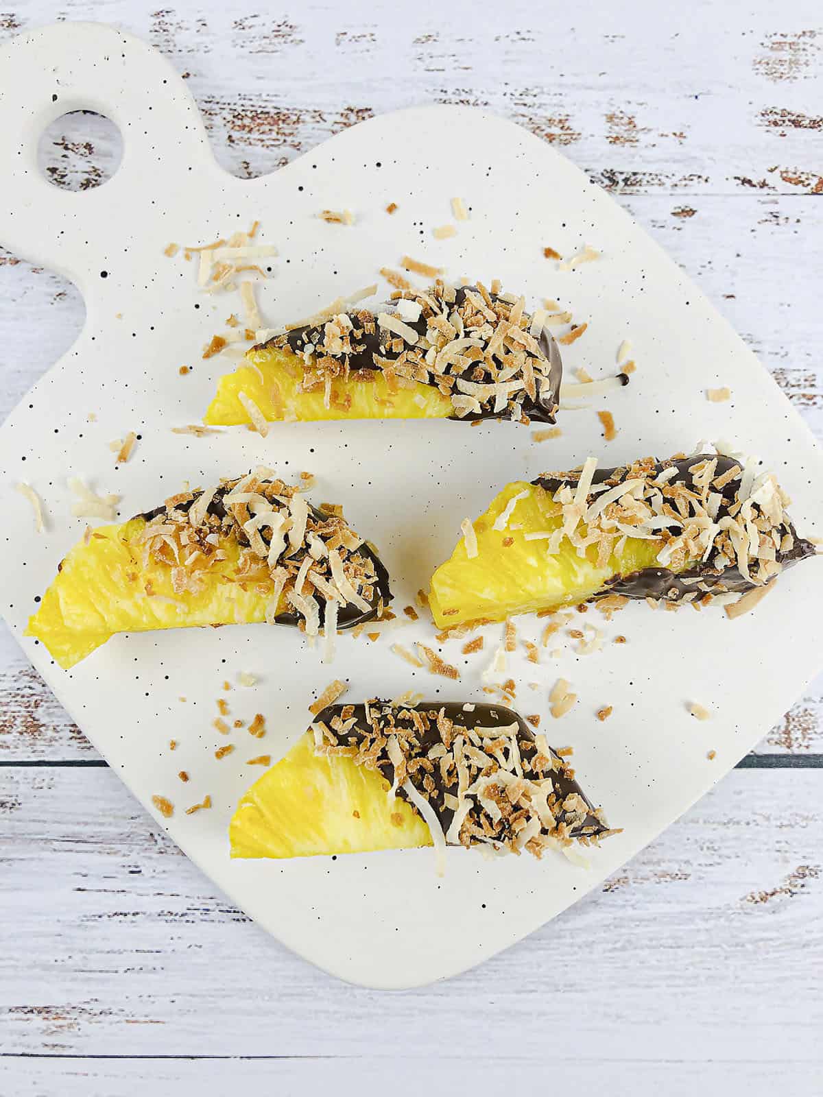 Pineapple spears with chocolate and coconut on a speckled serving tray.