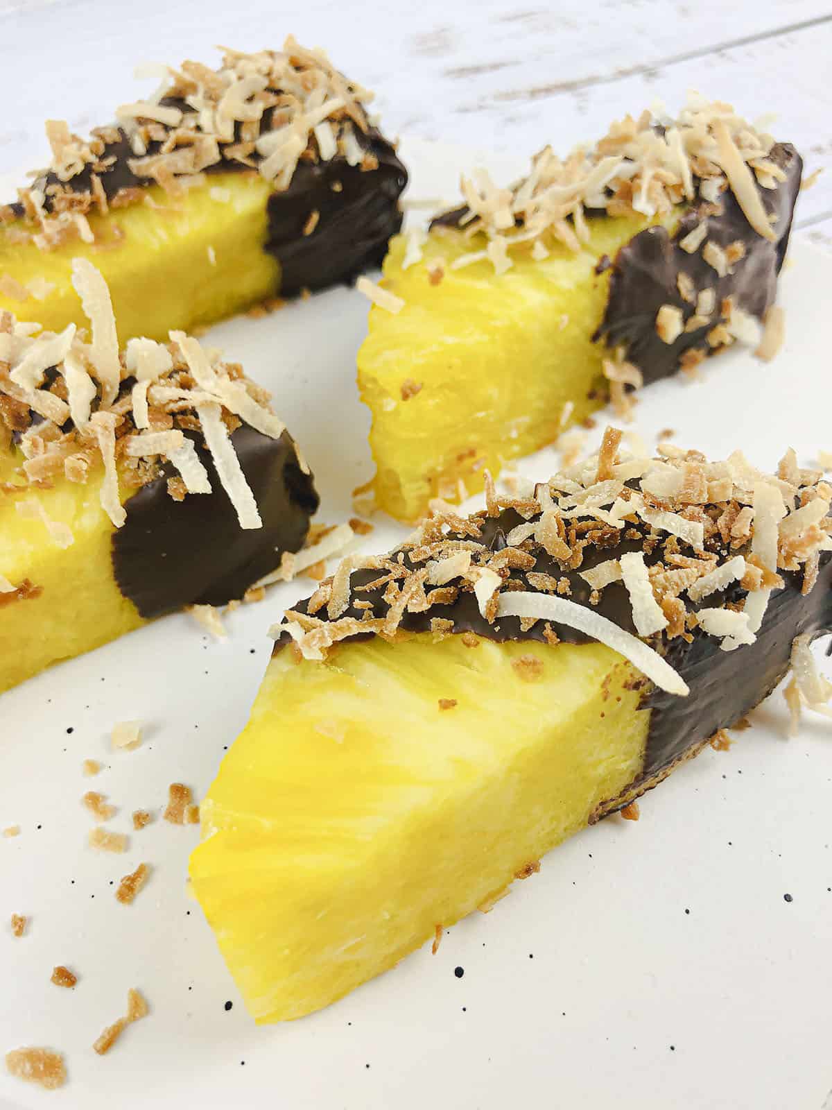 4 Chocolate dipped pineapple spears on a cutting board.