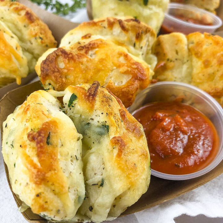 Cheesy garlic knots in a container with marinara dipping sauce.