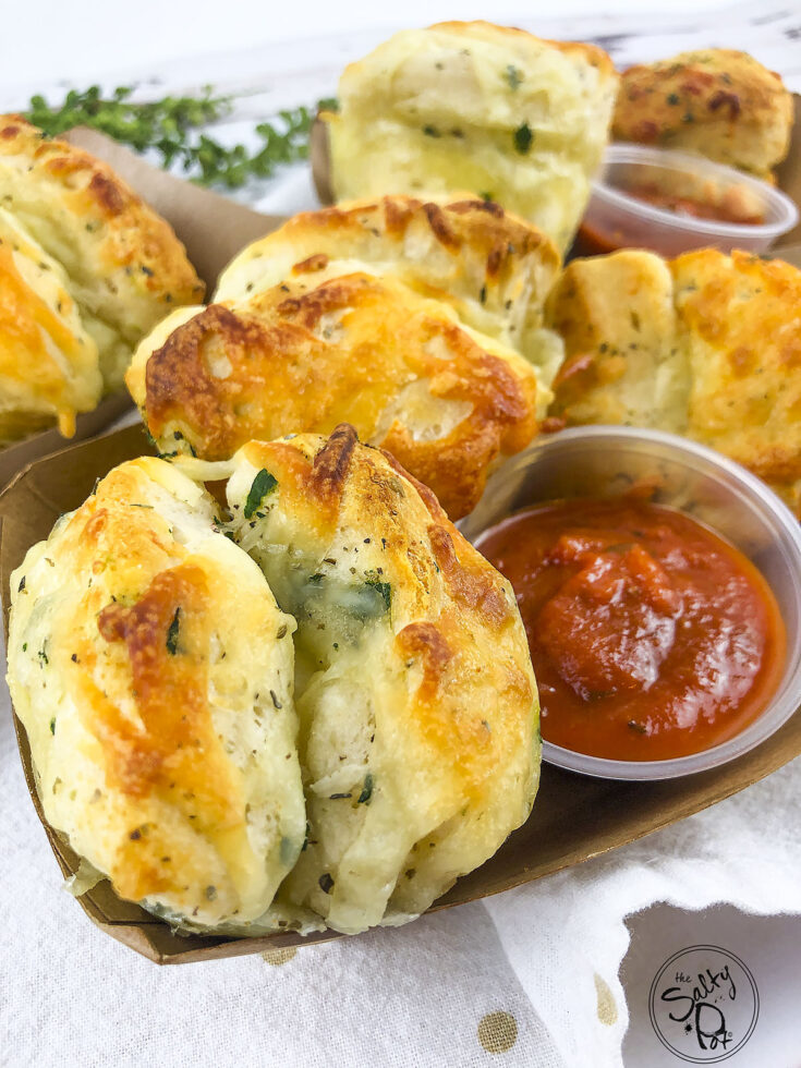 Cheesy garlic knots in a container with marinara dipping sauce.