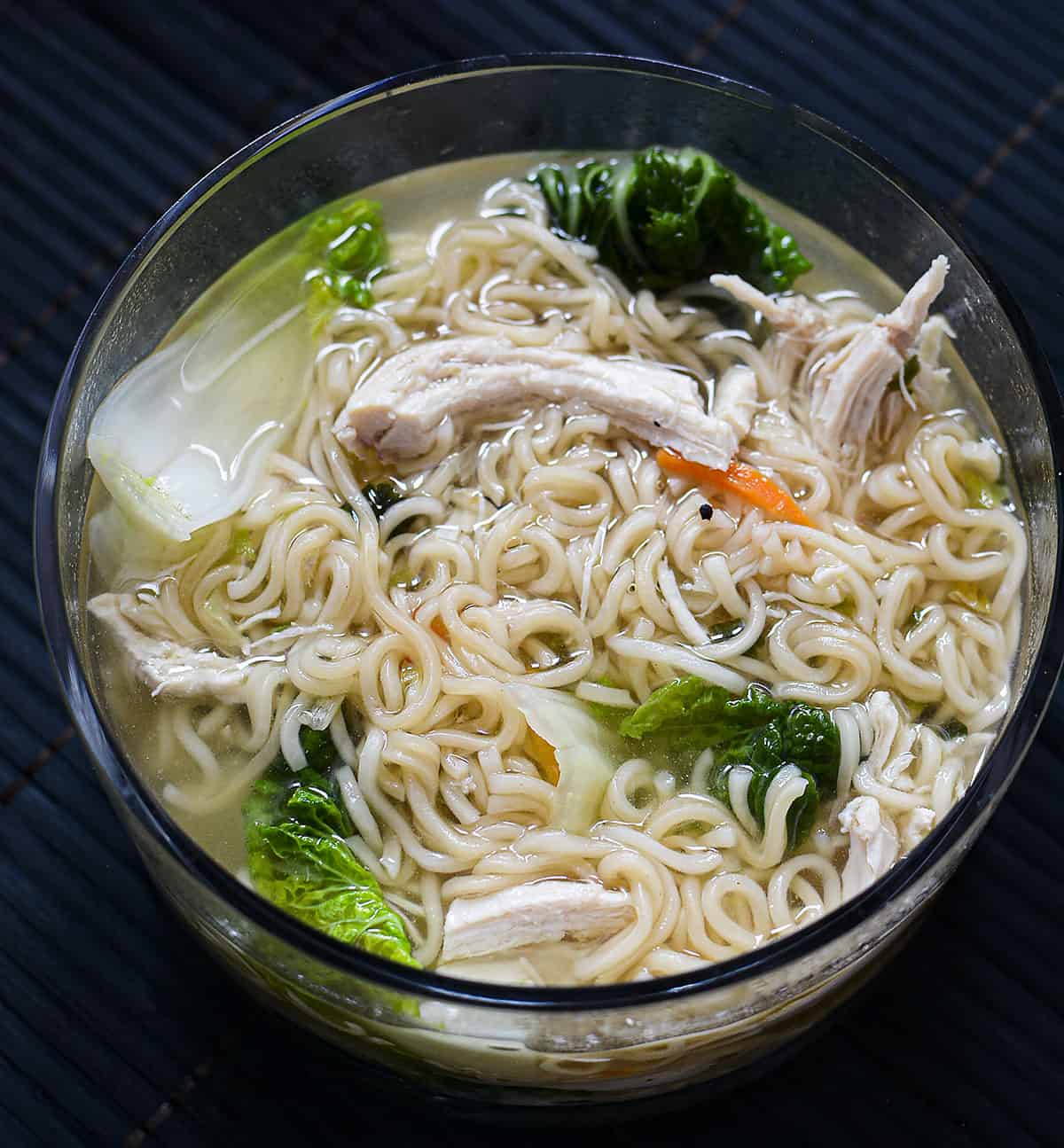 Ramen soup in a round glass bowl on a black background.