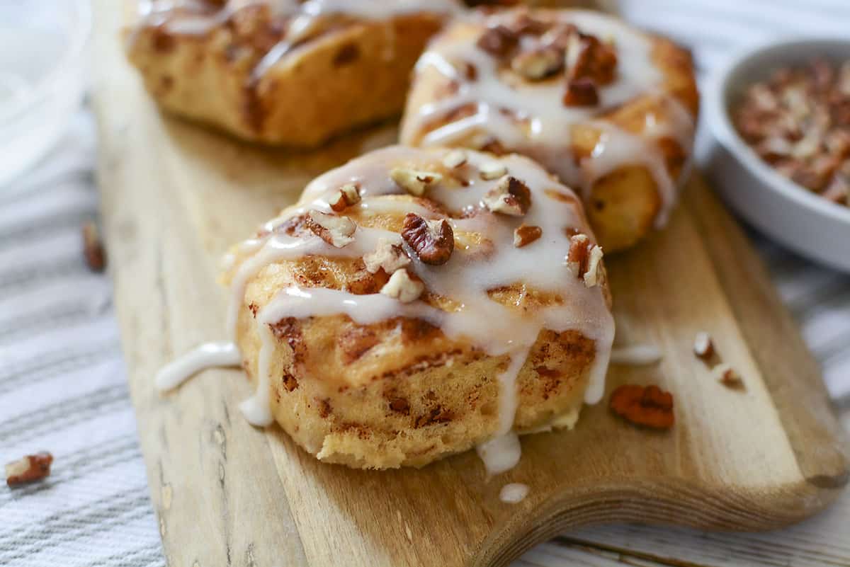 A cinnamon bun with glaze and pecans on top. Other rolls are in the background.