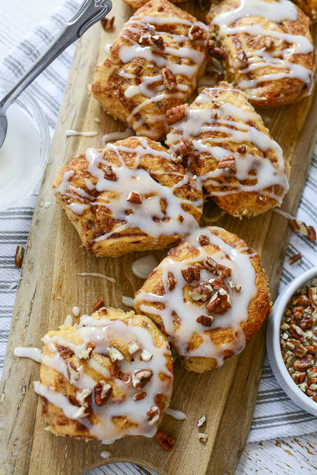 All the tiktok cinnamon rolls recipe are on a board with pecans in a dish on the right.