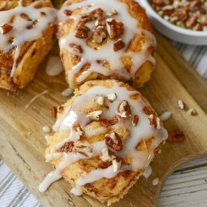 Some cinnamon rolls photographed from overhead. All the rolls have icing and pecans on them.