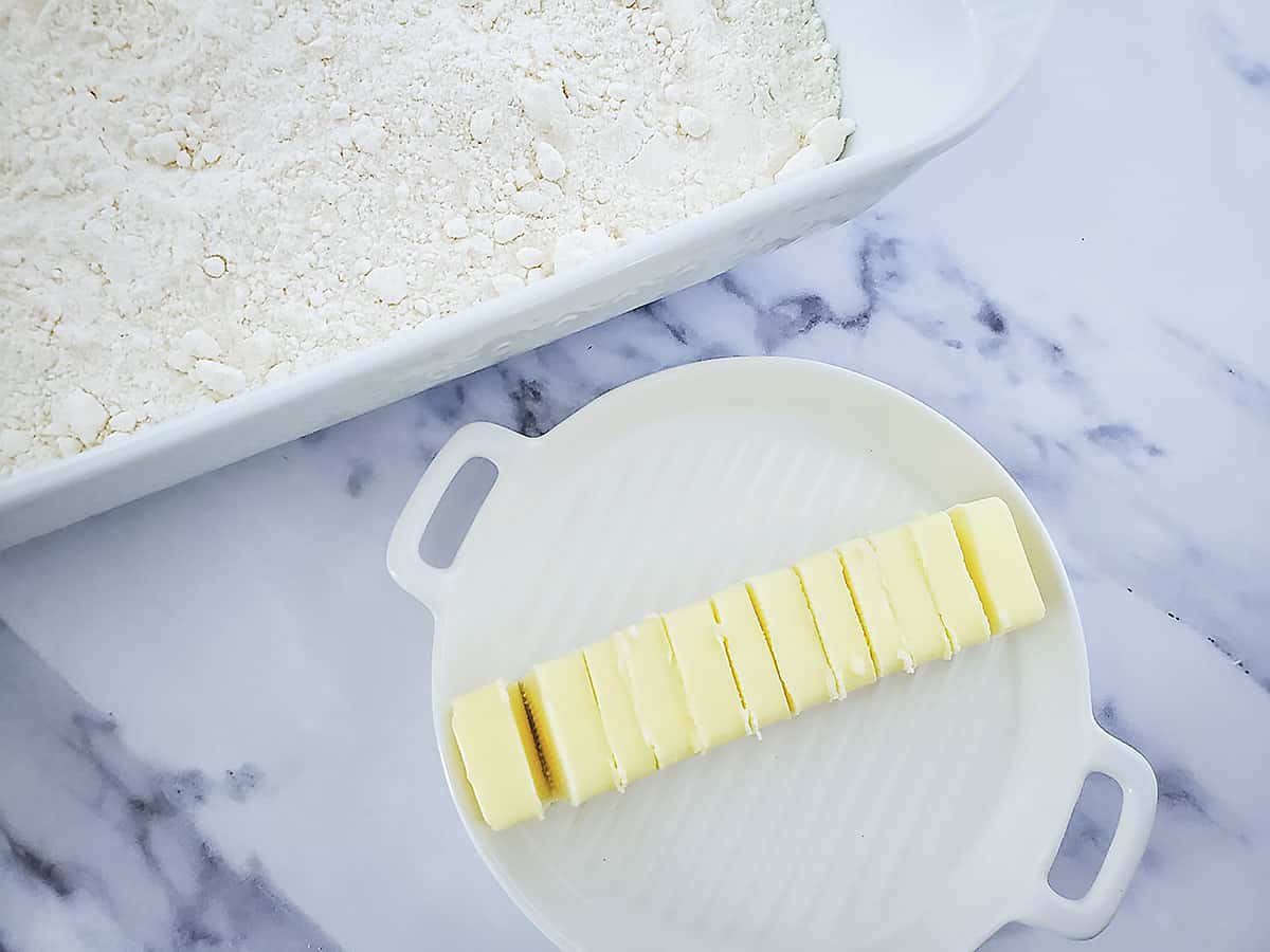 A stick of butter that's been sliced into 12 slices on a small white plate.