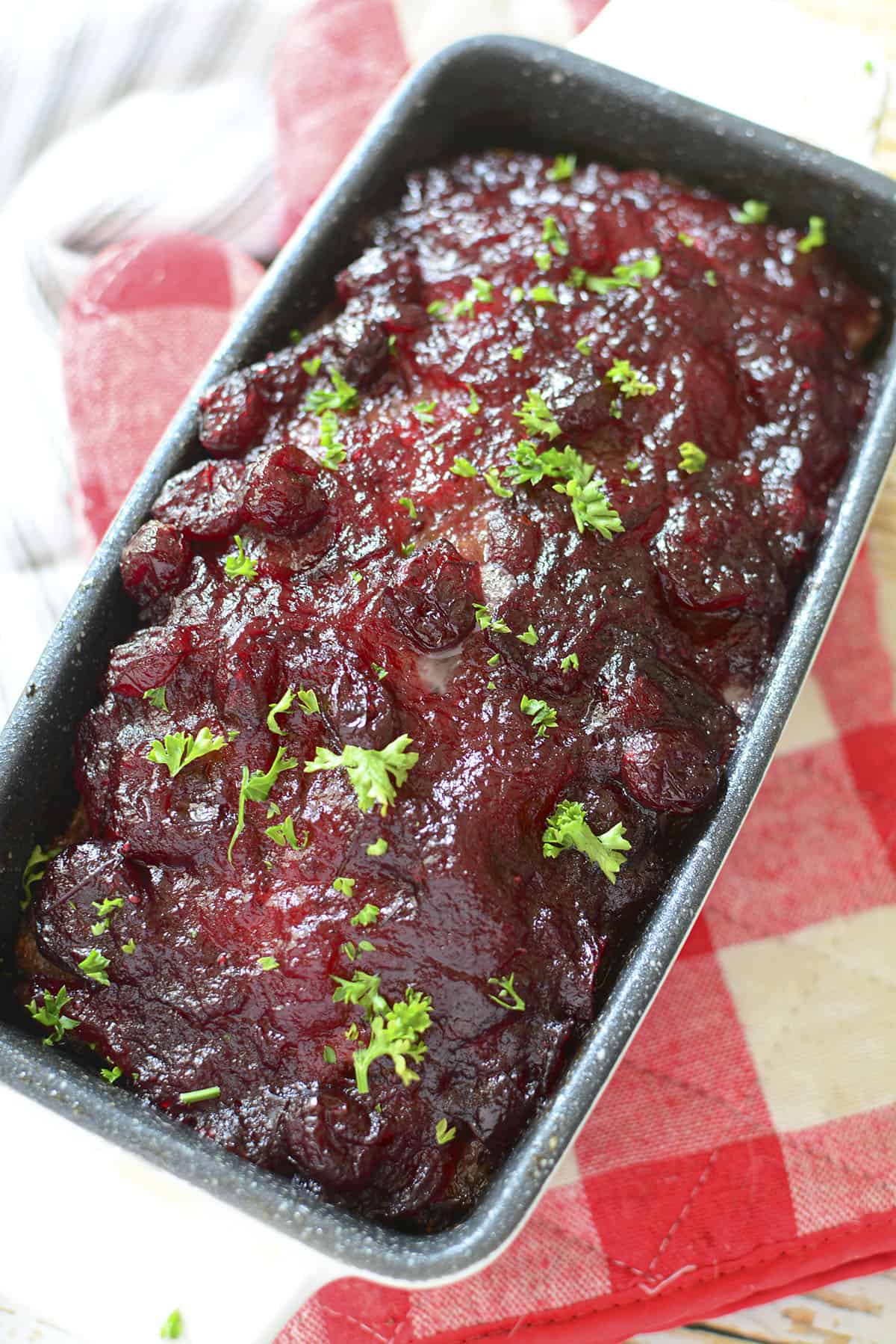 The turkey meatloaf with cranberry sauce spread over top and sprinkled with fresh green parsley.