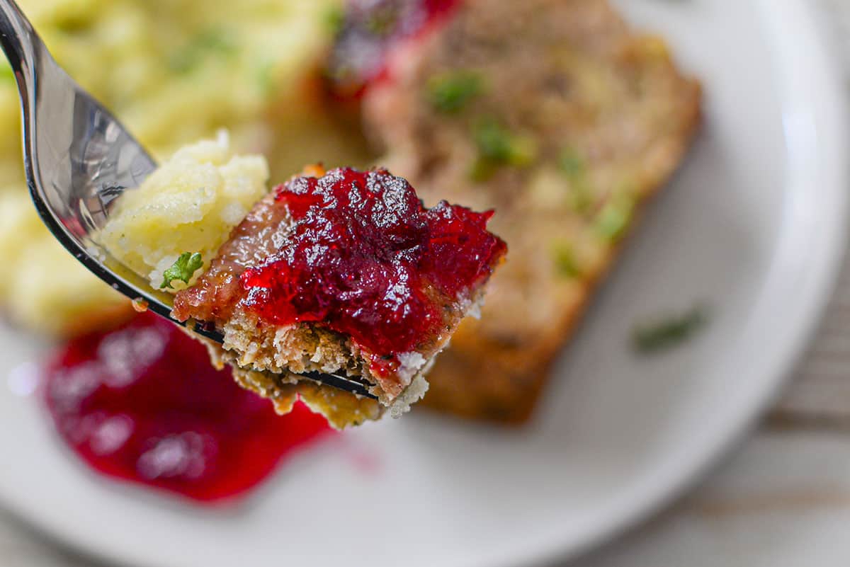 A forkfull of the meatloaf with mashed potatoes and cranberry sauce.