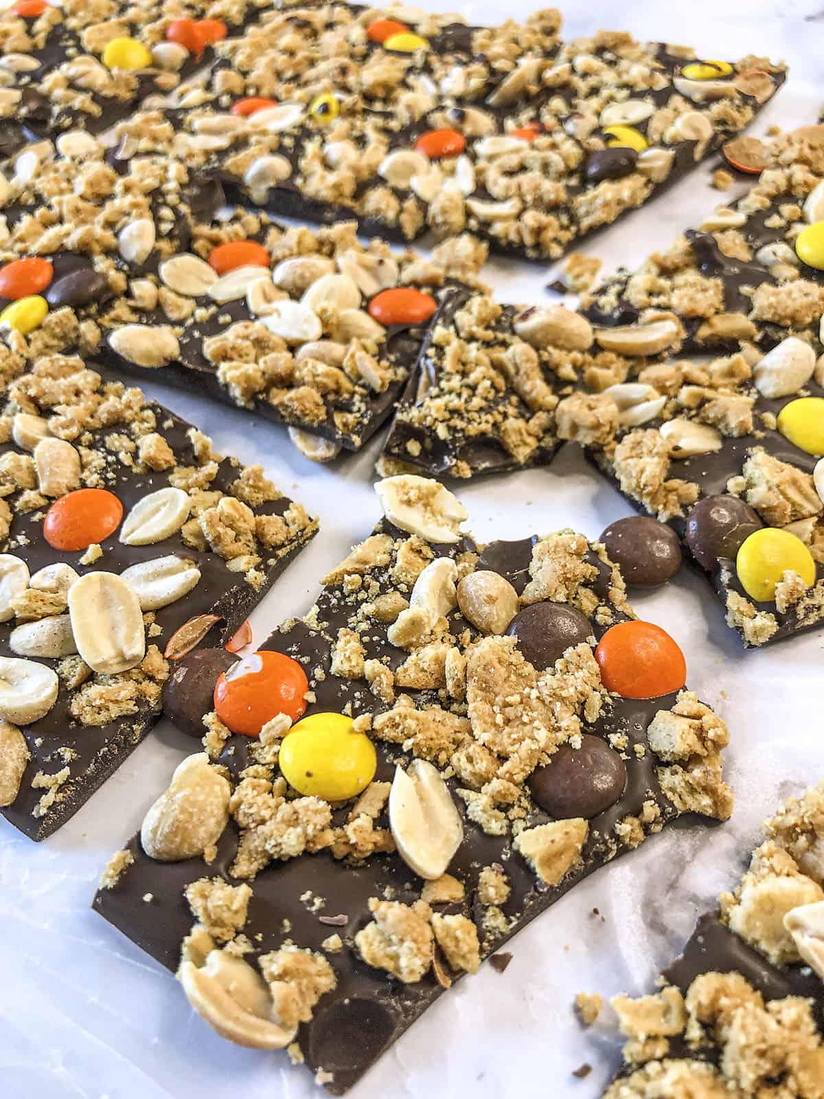 A close up photo of a piece of peanut butter bark with the ingredients showing, like orange and  yellow reese's pieces. 