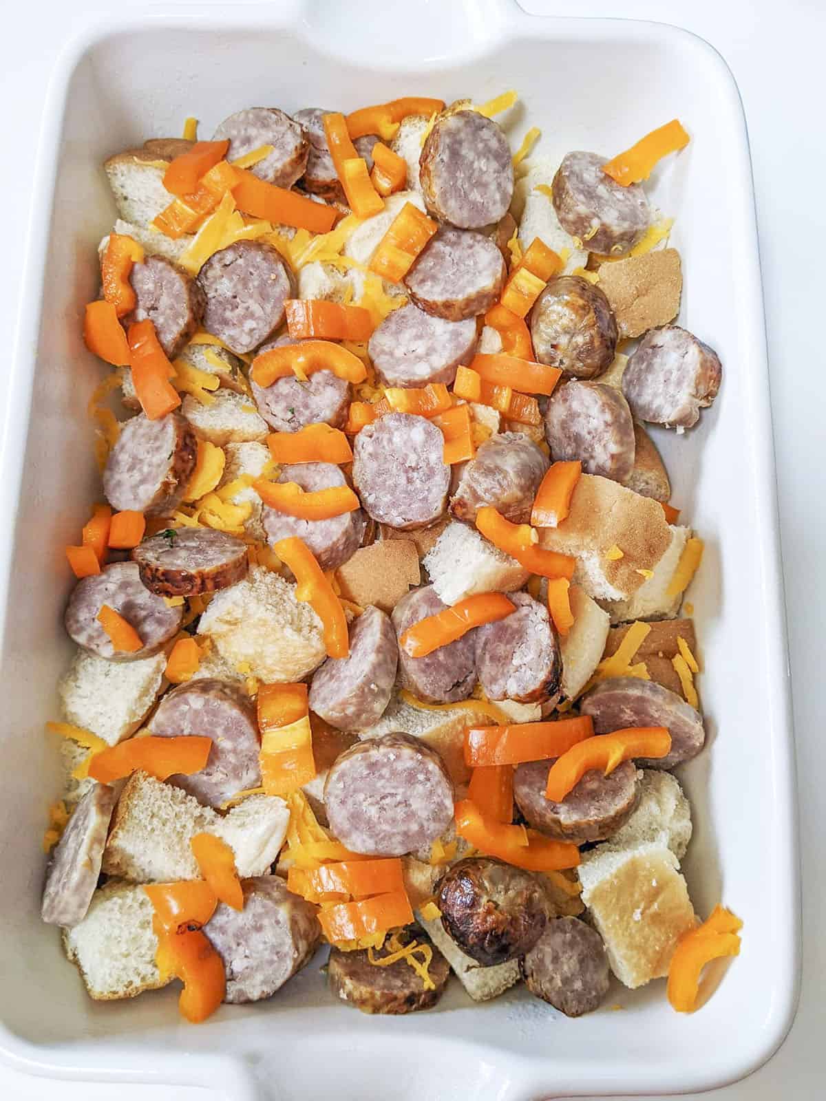 The dry ingredients such as sausage, bread, peppers and cheese in the casserole dish, waiting for the egg mixture.