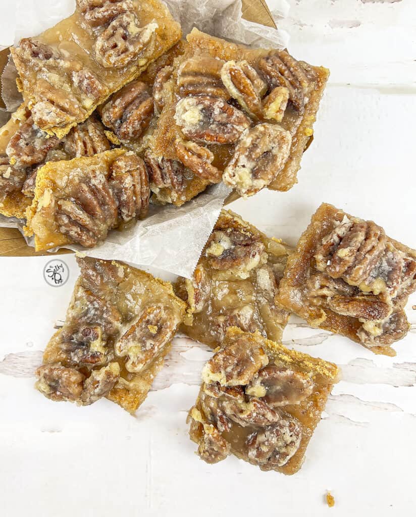 4 Pieces of pecan pie bark on the table with a container of the bark on the upper left.
