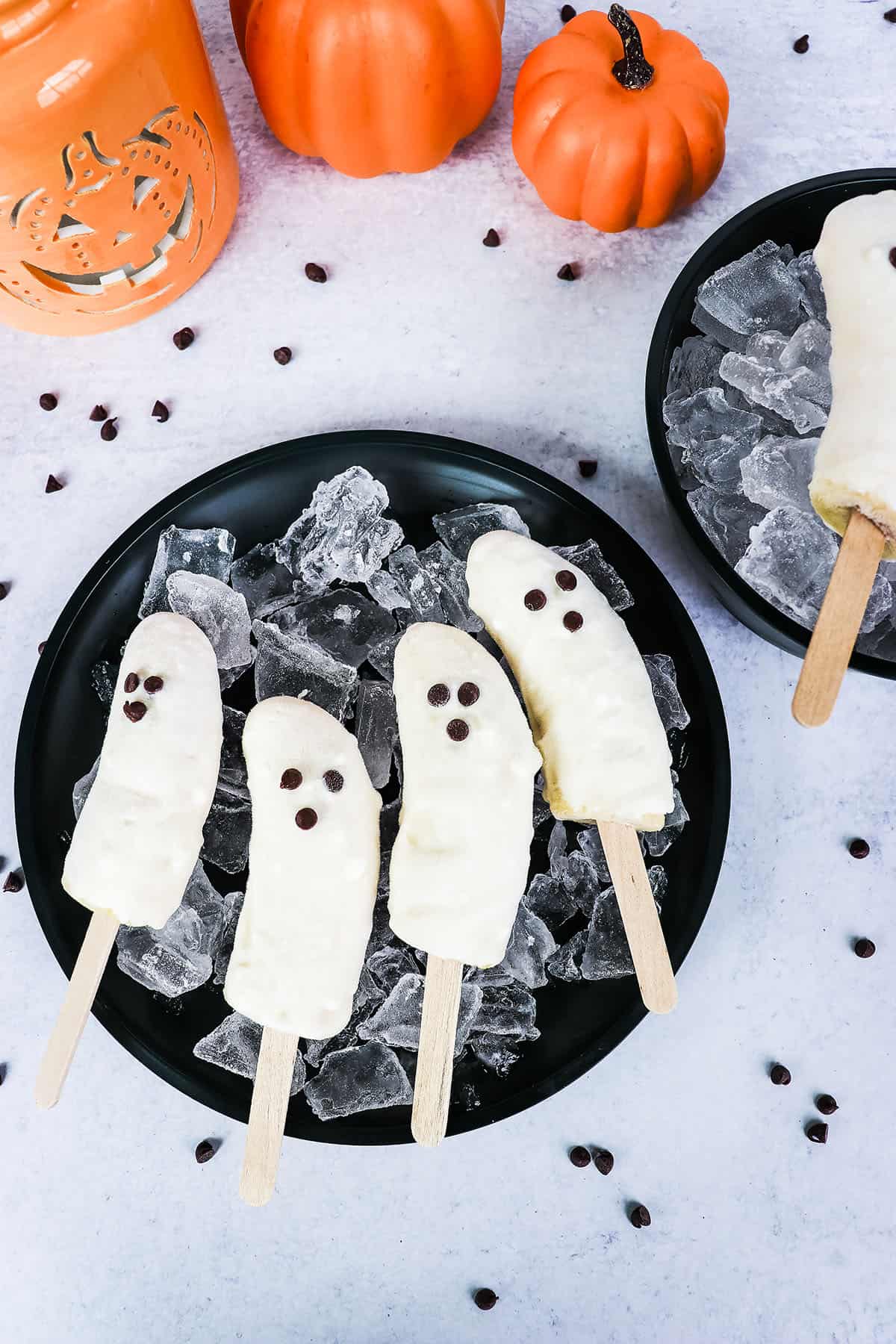 4 Banana pops sitting in a black dish with chocolate chips scattered around.
