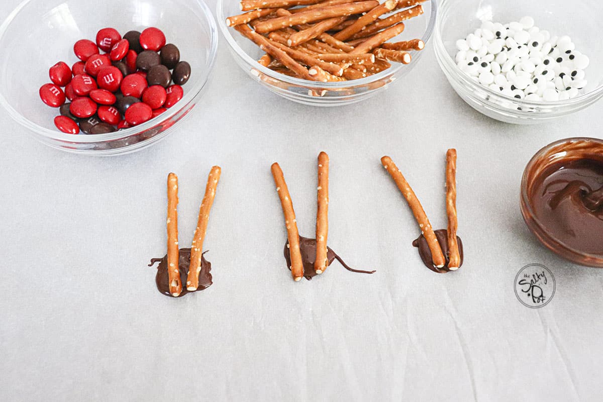 Three dabs of chocolate acting like glue with pretzel sticks for antlers.