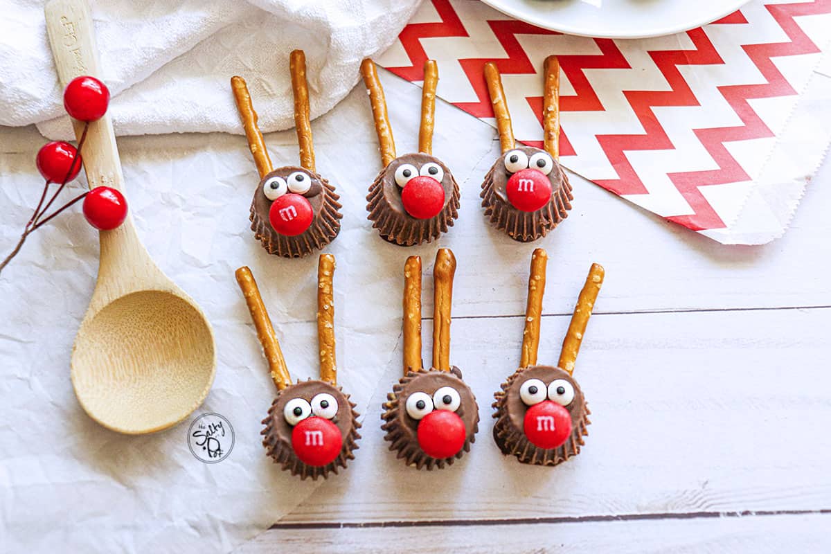 6 Rudolph christmas candies lined up with red chevron paper on the right and a wooden spoon on the left.