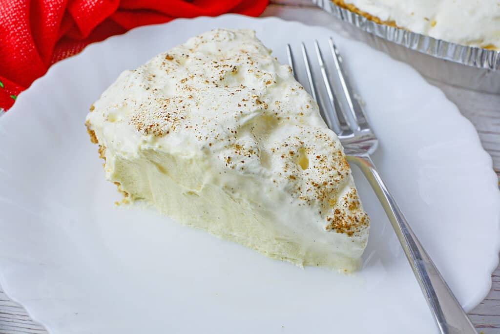 A slice of eggnog pie on a white plate with a fork on the right, next to the slice.