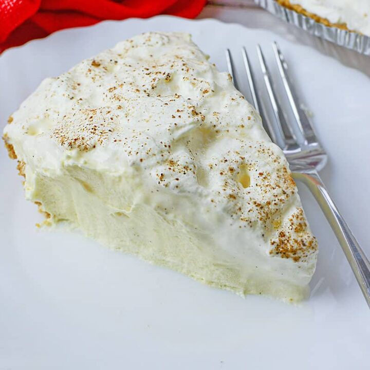 A slice of eggnog pie on a white plate with a fork on the right, next to the slice.