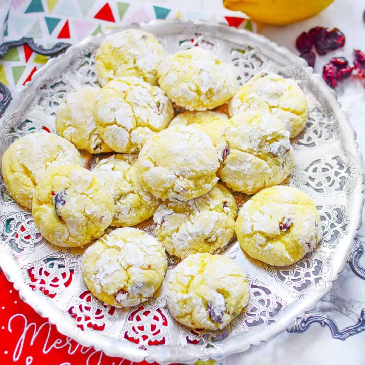 4 Ingredient Lemon Cranberry Cookies on a silver plate with a lemon and cranberries on the table on the upper right.