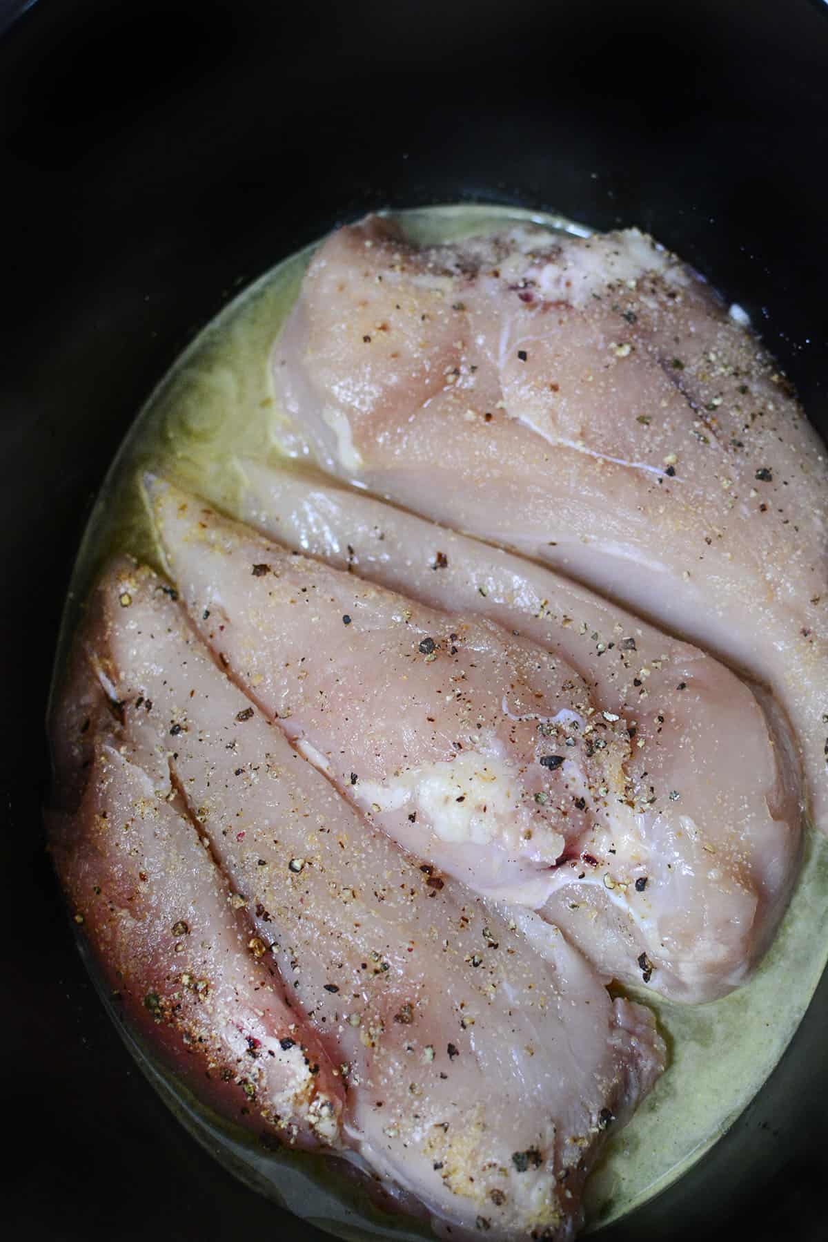 3 chicken breasts that are seasoned sitting in the slow cooker with chicken broth. 