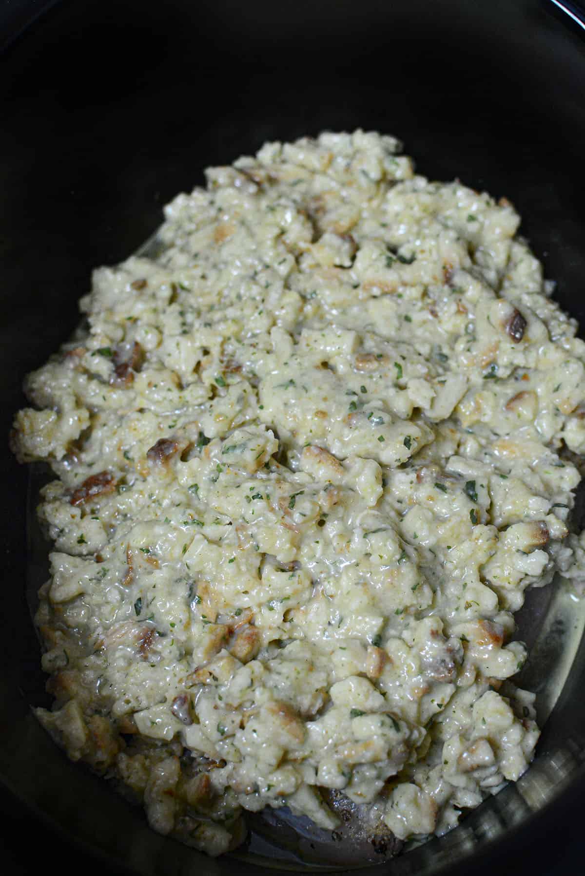 The stuffing mixture has been spread over top the chicken breasts in the slow cooker.