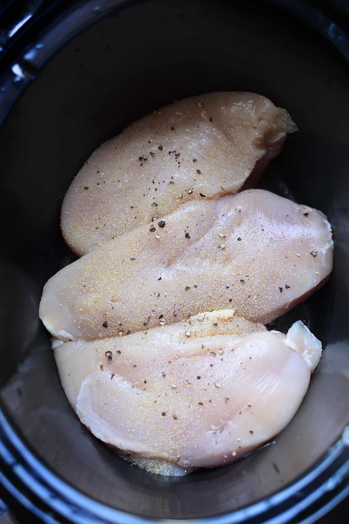 Three seasoned chicken breasts sit in a black crockpot. 