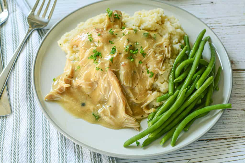 3 ingredient crockpot shredded chicken and gravy on a cream colored plate.