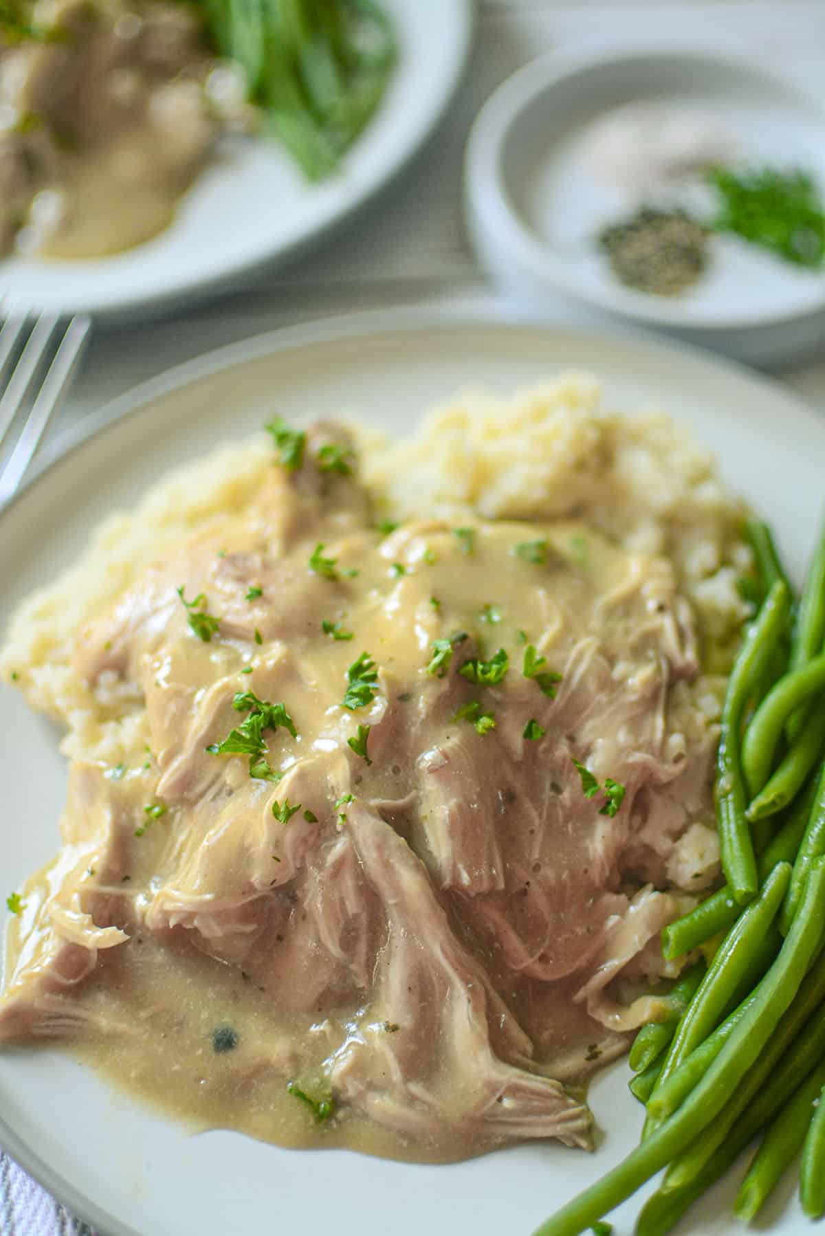 Chicken and gravy sit on a plate with mashed potatoes and green beans. 